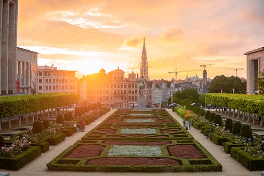 a European cityscape showing large buildings and a garden at sunset time